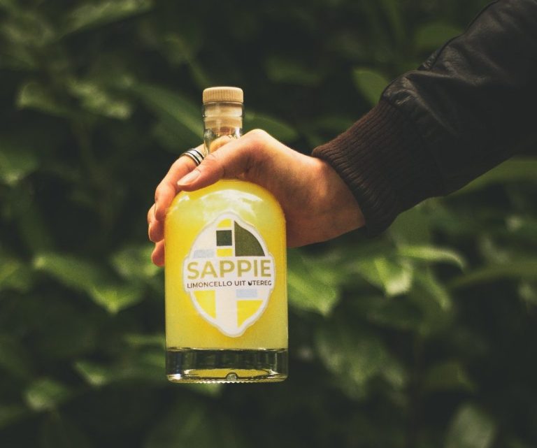 Een hand houdt een fles Sappie limoncello vast, met groene achtergronden.